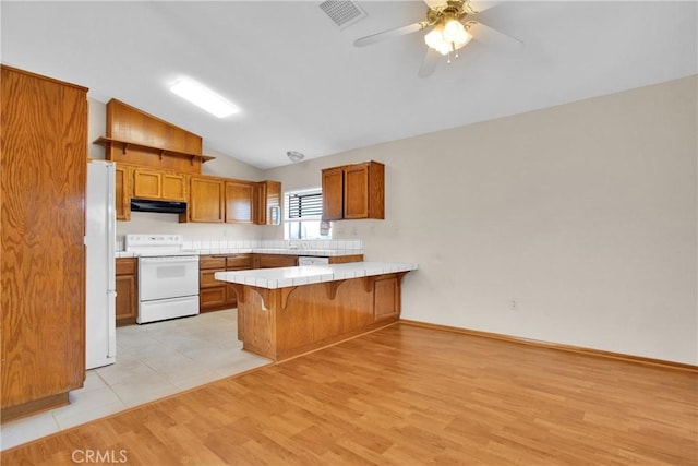 kitchen featuring ceiling fan, vaulted ceiling, tile countertops, kitchen peninsula, and white appliances