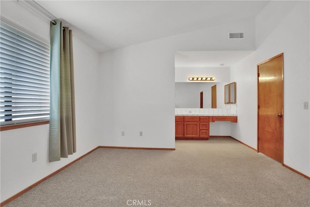 unfurnished bedroom with light carpet, vaulted ceiling, and connected bathroom