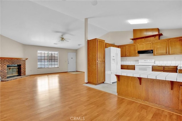 kitchen with tile countertops, range, white fridge with ice dispenser, a fireplace, and a kitchen breakfast bar