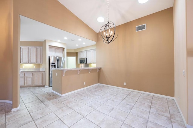 kitchen featuring appliances with stainless steel finishes, a kitchen bar, decorative light fixtures, light brown cabinetry, and light tile patterned floors