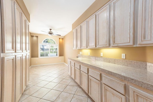 kitchen with light brown cabinetry, light stone counters, ceiling fan, and light tile patterned flooring