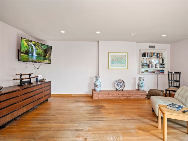 living room with built in shelves and light hardwood / wood-style flooring