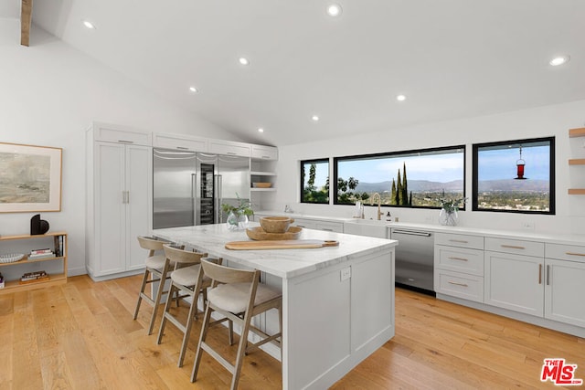 kitchen featuring white cabinetry, a breakfast bar area, appliances with stainless steel finishes, light stone counters, and a center island