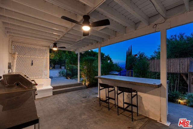 patio terrace at dusk featuring ceiling fan, a bar, and area for grilling