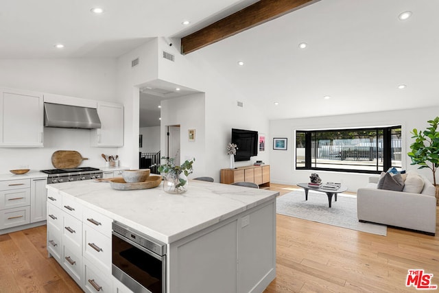 kitchen featuring a center island, beamed ceiling, stainless steel appliances, white cabinets, and wall chimney exhaust hood