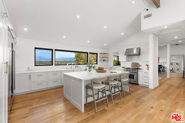 kitchen with wall chimney range hood, a kitchen island, white cabinetry, high end stainless steel range oven, and a breakfast bar area