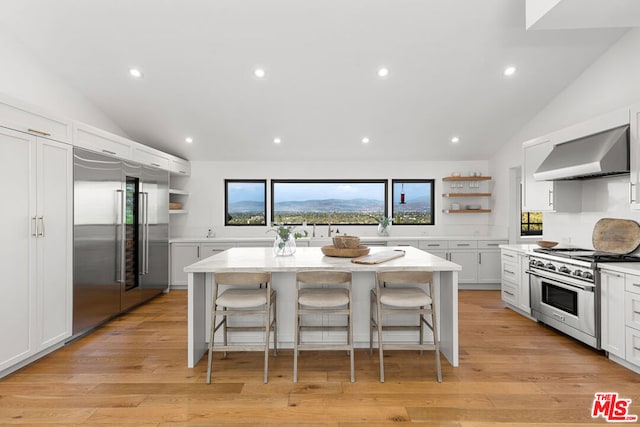 kitchen featuring a kitchen island, white cabinetry, premium appliances, a kitchen breakfast bar, and wall chimney exhaust hood