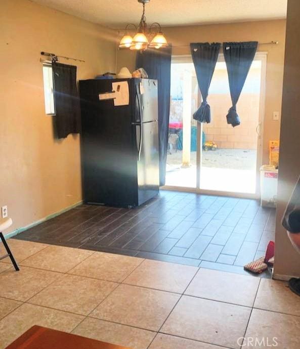 interior space featuring tile patterned flooring, a notable chandelier, pendant lighting, and black fridge