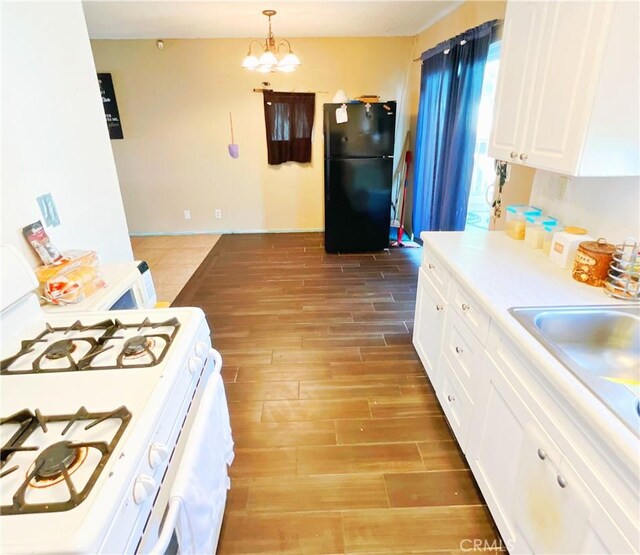 kitchen with white cabinetry, black refrigerator, a notable chandelier, white range with gas cooktop, and hanging light fixtures