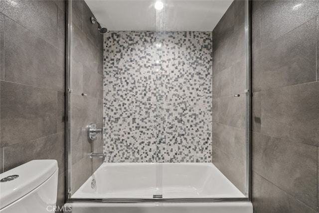 bathroom with bath / shower combo with glass door, toilet, and tile walls