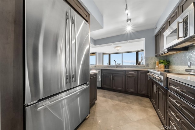 kitchen with light tile patterned floors, stainless steel appliances, backsplash, dark brown cabinets, and sink