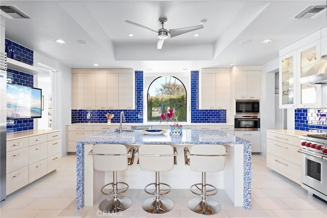 kitchen featuring tasteful backsplash, appliances with stainless steel finishes, a kitchen bar, and a center island with sink