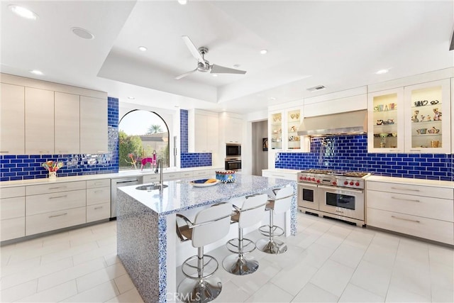 kitchen featuring a breakfast bar, a sink, ventilation hood, appliances with stainless steel finishes, and a raised ceiling