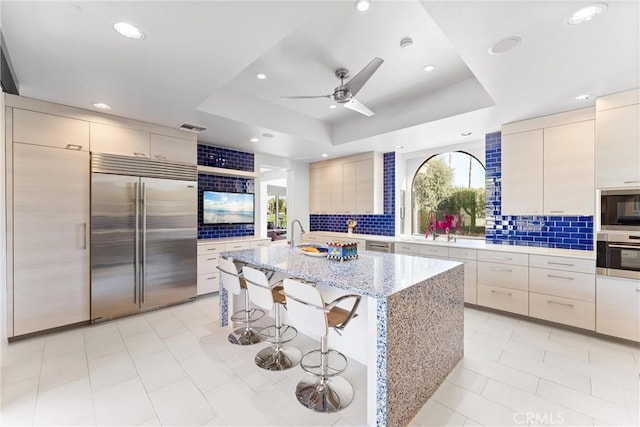 kitchen with tasteful backsplash, a breakfast bar area, a raised ceiling, and stainless steel built in fridge