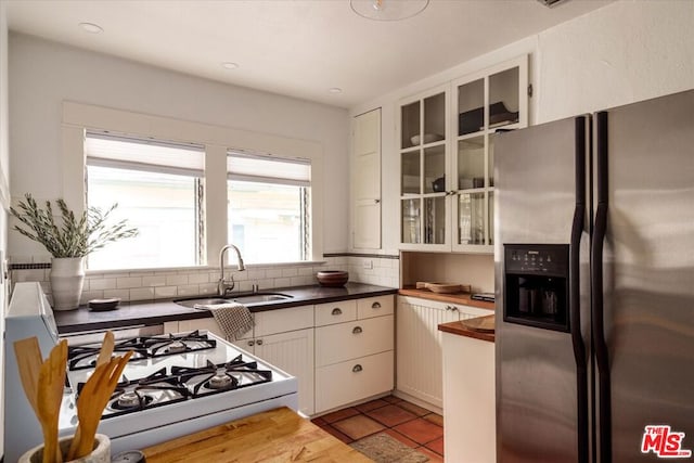 kitchen with light tile patterned floors, white cabinetry, stainless steel fridge, white range with gas cooktop, and sink