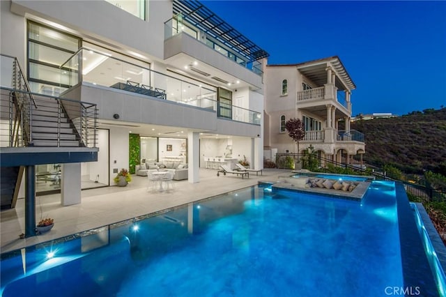 back of house at night featuring an in ground hot tub, a patio area, a fenced in pool, and stucco siding