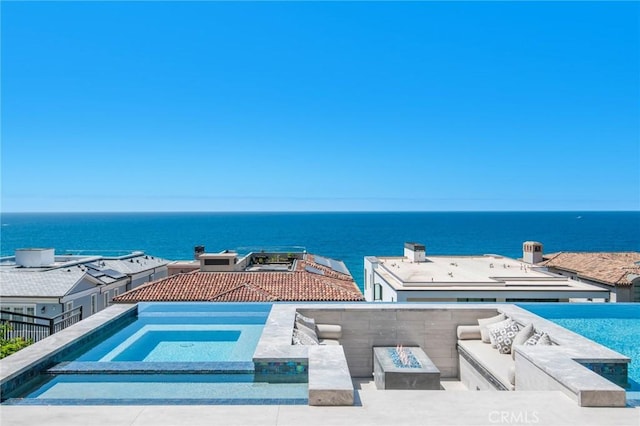 view of pool with a water view, an outdoor living space with a fire pit, and an in ground hot tub