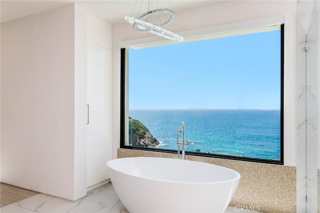 full bath featuring marble finish floor, a water view, and a freestanding bath