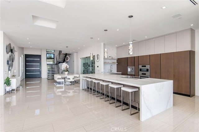 kitchen with light stone countertops, pendant lighting, a kitchen bar, double oven, and sink