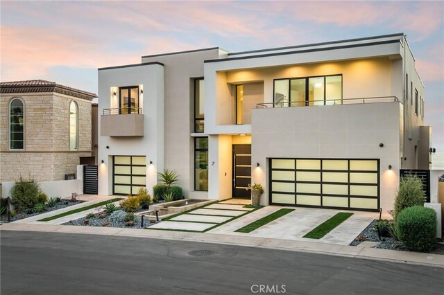 contemporary house featuring a balcony, an attached garage, concrete driveway, and stucco siding