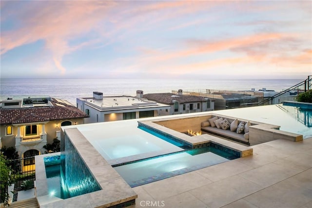 pool at dusk with pool water feature, an in ground hot tub, and a water view