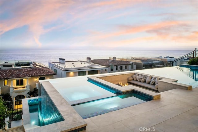 pool at dusk featuring a water view, a pool with connected hot tub, and a patio