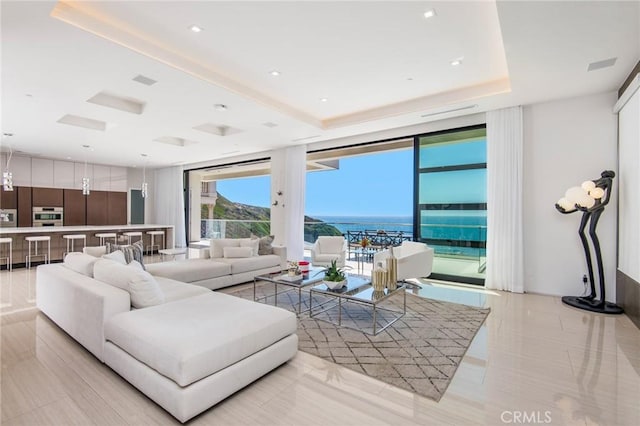 living area featuring a water view, a tray ceiling, and a wall of windows