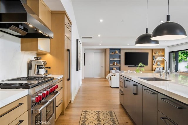 kitchen featuring wall chimney exhaust hood, range with two ovens, sink, hanging light fixtures, and light hardwood / wood-style flooring