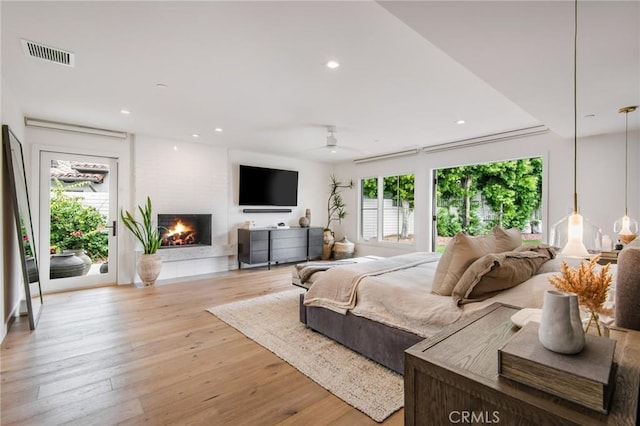 bedroom featuring ceiling fan, light wood-type flooring, access to outside, and a fireplace