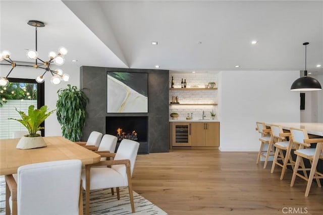 dining area with beverage cooler, lofted ceiling, a premium fireplace, sink, and light wood-type flooring