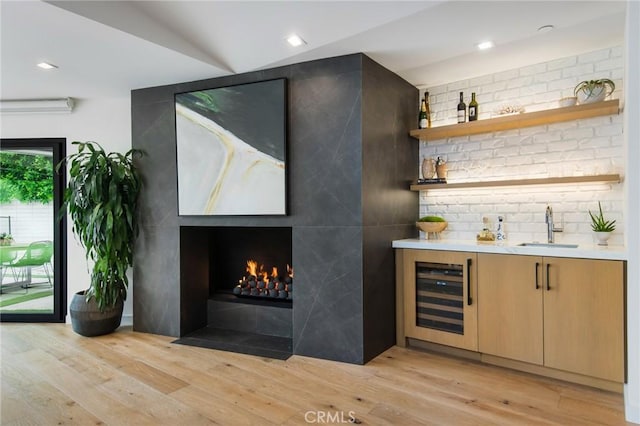 bar featuring lofted ceiling, a fireplace, beverage cooler, light hardwood / wood-style flooring, and sink