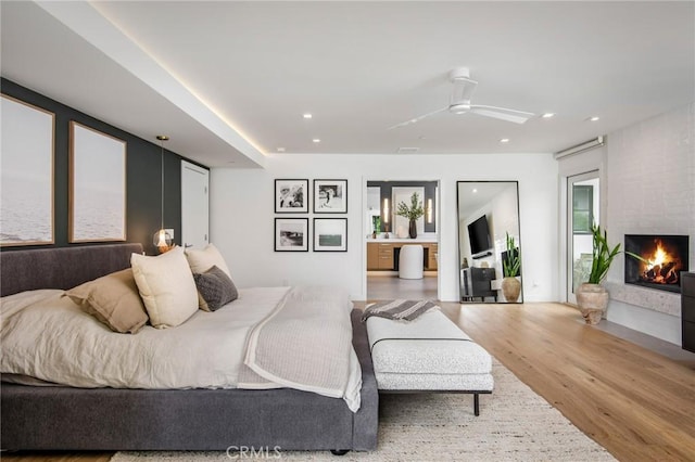 bedroom with ceiling fan, a large fireplace, hardwood / wood-style floors, and multiple windows