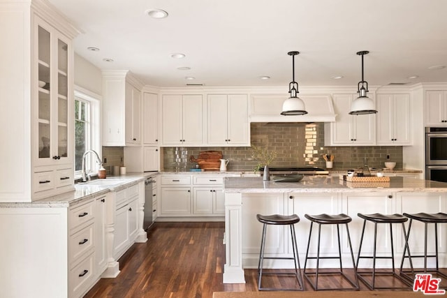 kitchen with sink, hanging light fixtures, a kitchen island with sink, white cabinets, and dark hardwood / wood-style flooring