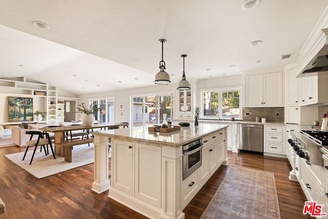 kitchen featuring lofted ceiling, tasteful backsplash, a center island, light stone countertops, and appliances with stainless steel finishes