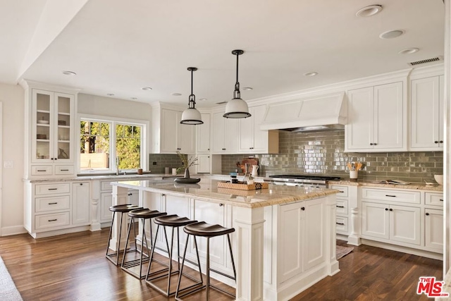 kitchen featuring dark hardwood / wood-style floors, premium range hood, white cabinets, and a kitchen island with sink