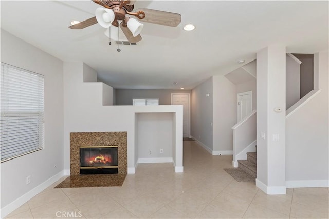 unfurnished living room featuring a premium fireplace, light tile patterned floors, and ceiling fan