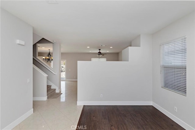 tiled empty room featuring ceiling fan with notable chandelier