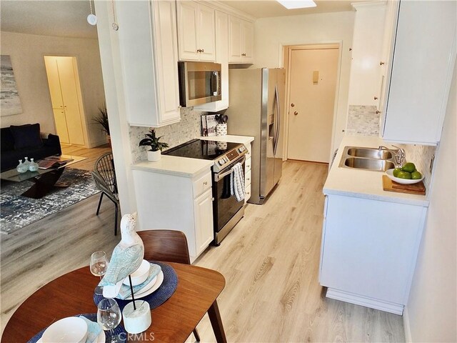 kitchen with light hardwood / wood-style flooring, backsplash, white cabinets, appliances with stainless steel finishes, and sink