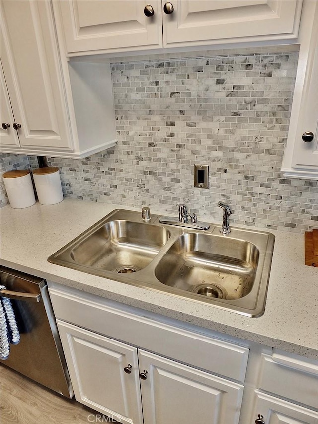 kitchen featuring white cabinetry, decorative backsplash, light wood-type flooring, stainless steel dishwasher, and sink