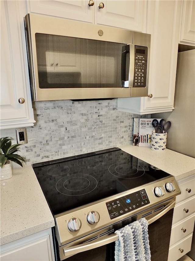 kitchen featuring white cabinetry, stainless steel appliances, tasteful backsplash, and light stone countertops