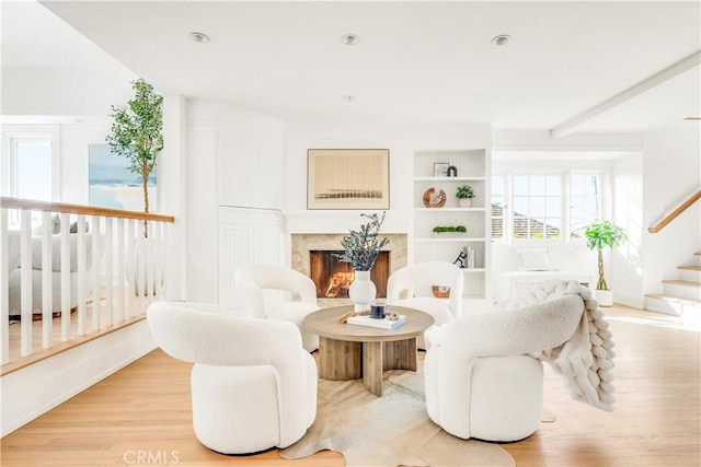 sitting room featuring built in features, a fireplace, and light hardwood / wood-style flooring