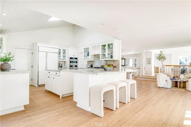 kitchen featuring a center island, lofted ceiling, white cabinetry, backsplash, and light wood-type flooring