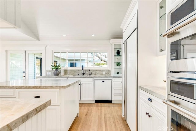 kitchen with white cabinetry, stainless steel double oven, sink, light hardwood / wood-style flooring, and dishwashing machine