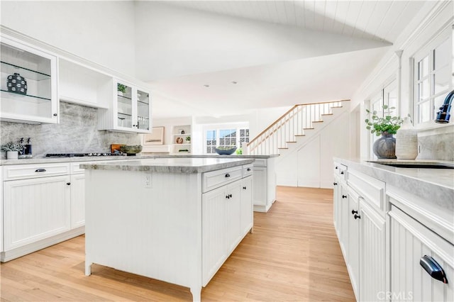 kitchen with light wood-type flooring, a center island, white cabinetry, tasteful backsplash, and vaulted ceiling