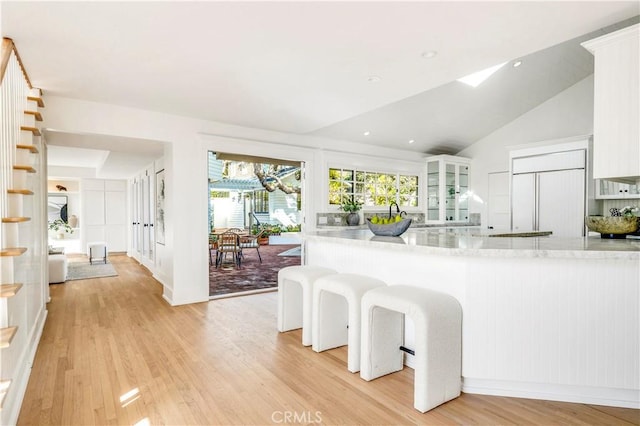 kitchen featuring white cabinetry, kitchen peninsula, paneled fridge, lofted ceiling, and light hardwood / wood-style flooring