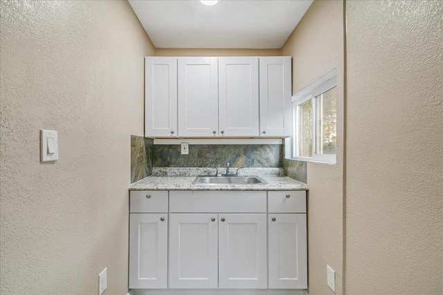 kitchen with light stone countertops, sink, decorative backsplash, and white cabinets