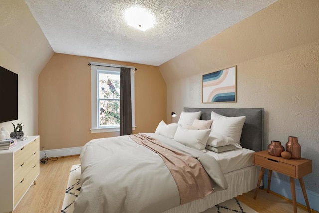 bedroom with vaulted ceiling, a textured ceiling, and light wood-type flooring