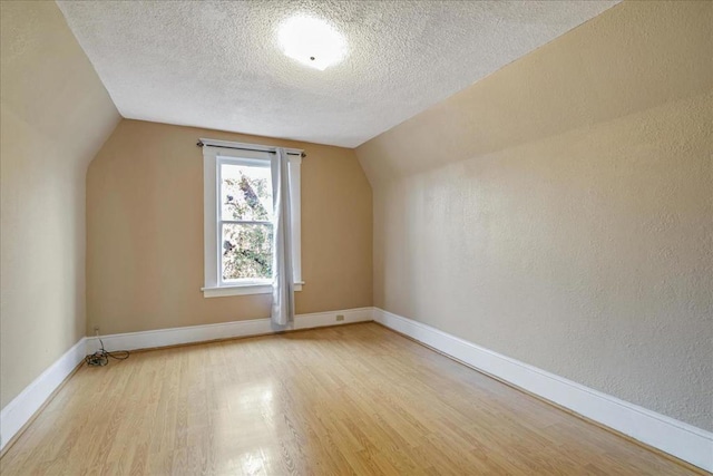 additional living space featuring vaulted ceiling, light hardwood / wood-style flooring, and a textured ceiling