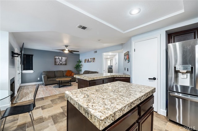 kitchen with stainless steel fridge with ice dispenser, ceiling fan, dark brown cabinets, and a center island