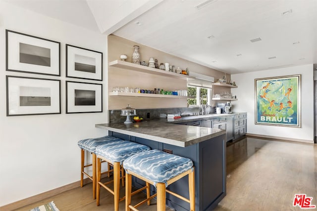 kitchen featuring sink, kitchen peninsula, hardwood / wood-style flooring, and a kitchen bar